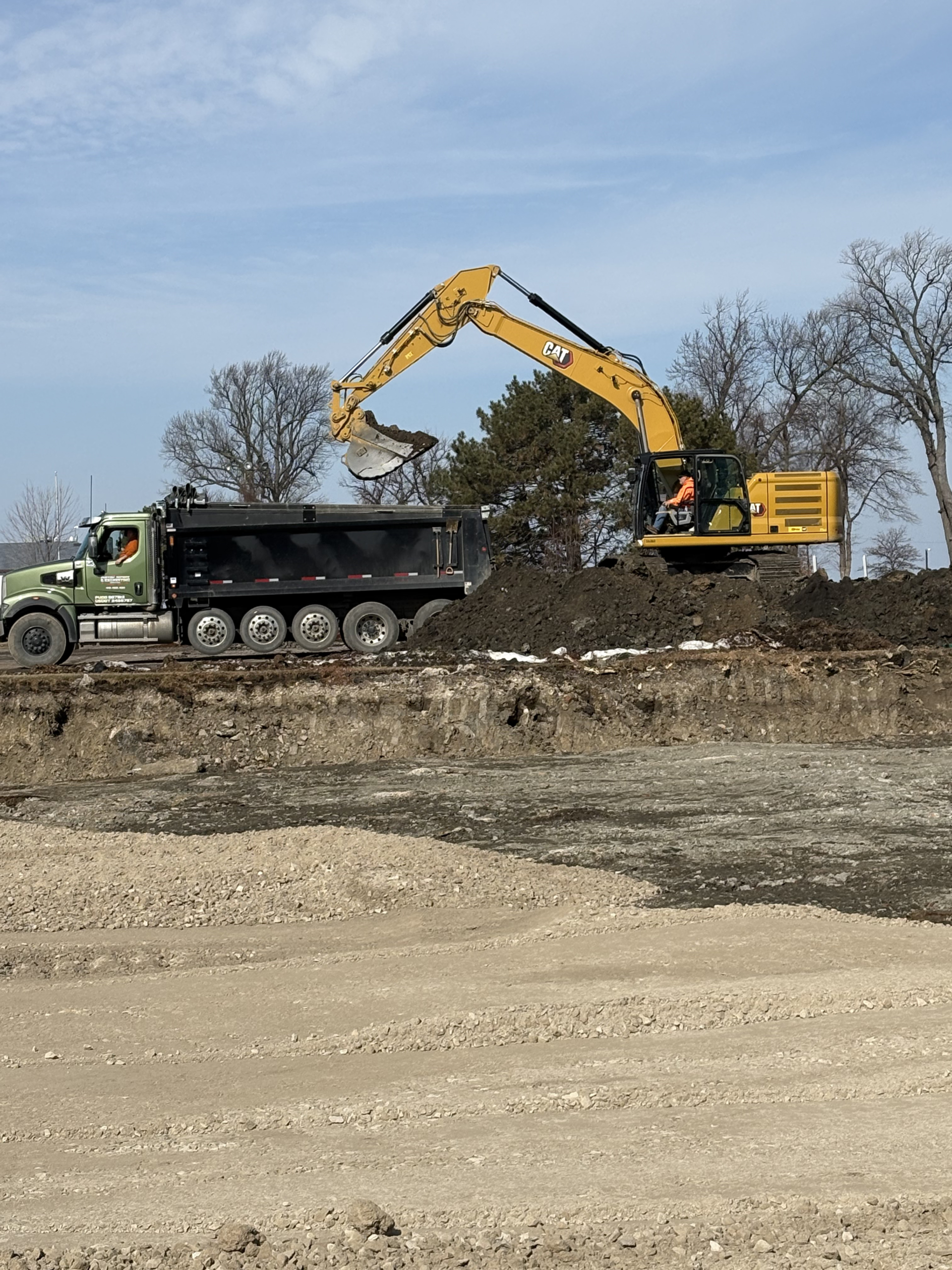 Excavator loading lead- and PAH-impacted soil into a dump truck for off-site disposal during waterfront marina soil remediation
