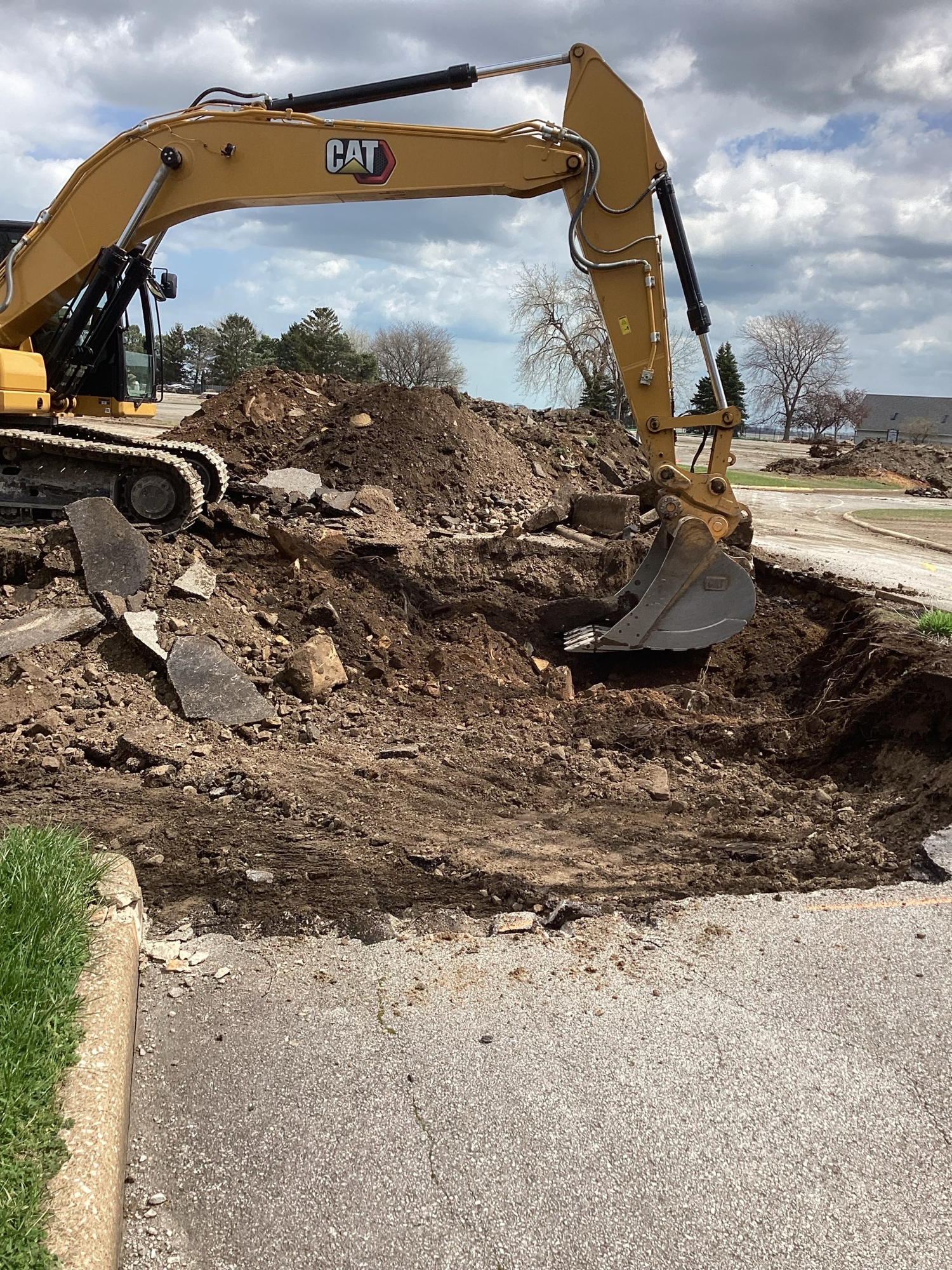 Excavator removing broken asphalt and digging out impacted soil beneath old pavement during marina site remediation and demolition